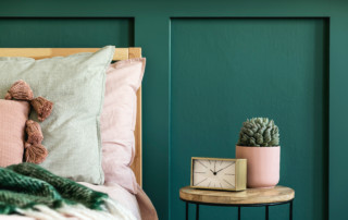 Bedroom with pastel bedding and wooden table beside it with clock and plant