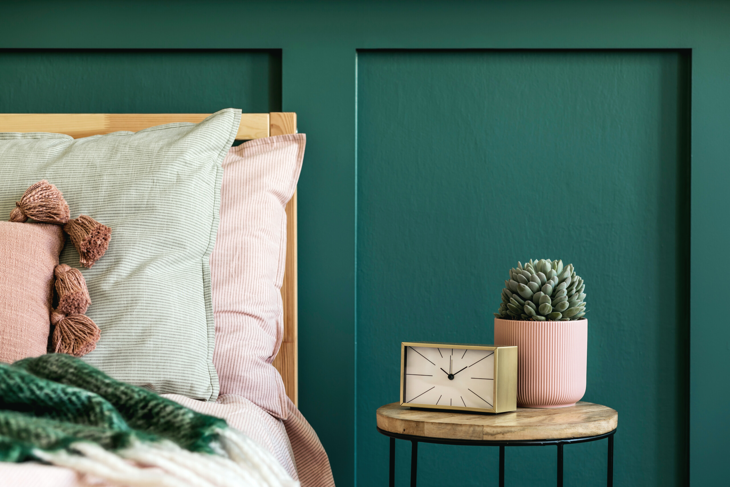 Bedroom with pastel bedding and wooden table beside it with clock and plant