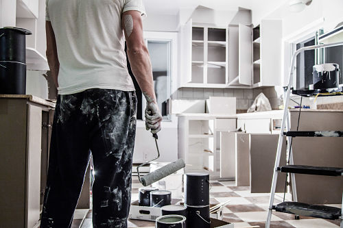 Man in jeans and white shirt painting kitchen cabinets