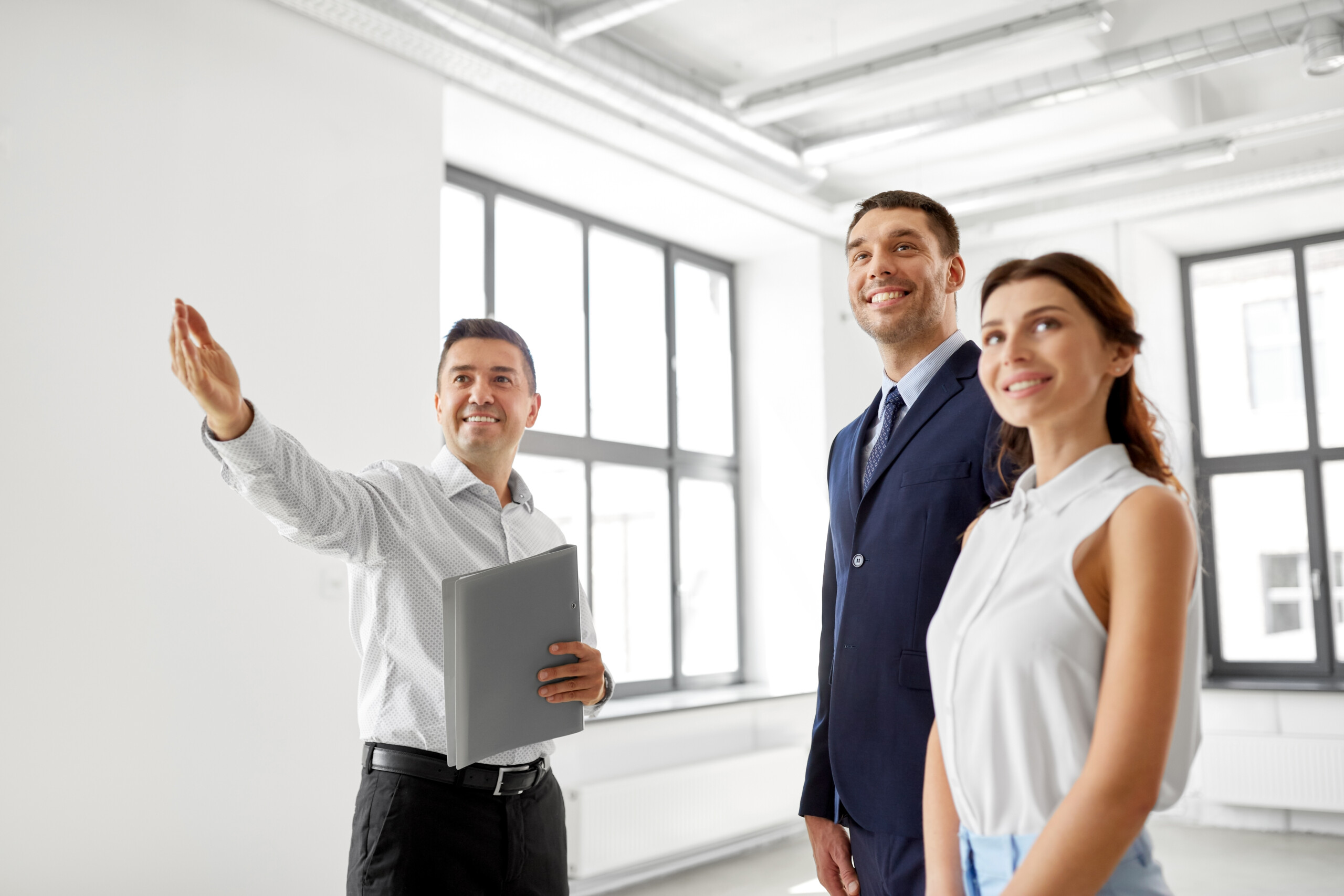 real estate business, sale and people concept - happy smiling realtor with folder showing new office room to customers