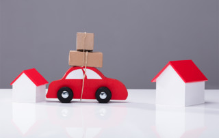 Block car and houses with boxes tied to the top of the car to depict moving from one home to the next