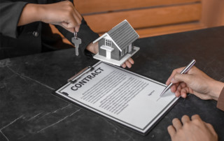 Man signing a contract while real estate agent holds out keys and figure of home