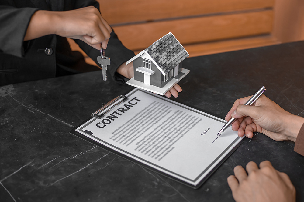 Man signing a contract while real estate agent holds out keys and figure of home